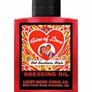 May include: A red glass bottle with a black cap. The label features a heart with the words "Aura of Love" and an image of a couple. The text "Old Southern Style" and "Dressing Oil" are also visible. The bottle is from Lucky Mojo Curio Co.