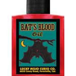 May include: A red glass bottle with a black cap and a label that reads "Bat's Blood Oil". The label features a black bat with red eyes hanging from a branch with a crescent moon in the background. The label also includes the text "Lucky Mojo Curio Co., 4618 Geary Blvd., San Francisco, Calif."