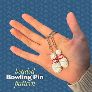 May include: Two miniature bowling pin charms crafted from small white beads with red horizontal stripes near the neck. Each pin is attached to a silver-toned metal split ring keychain by a short silver chain. The charms are held in an open palm.