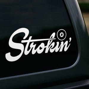 Puede incluir: Calcomanía de vinilo blanco con la palabra "Strokin'" en fuente cursiva, acompañada de un taco de billar y una bola número 8. Diseñada para ser aplicada en la ventana de un coche o superficie similar.