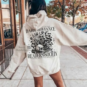 May include: Cream hoodie with a back graphic of a skull, snake, roses, and the text "DARK ROMANCE READERS SOCIETY". The design includes the text "Enemies to Lovers" and "Trigger Warnings Welcome".