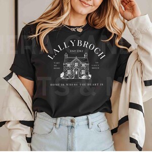 May include: Black t-shirt with a white graphic design featuring a house with the text "Lallybroch Est 1702" and "Take me home to Lallybroch. Home is where the heart is."
