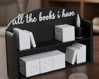 May include: Black bookshelf with the text "all the books i have" in white script. The shelf holds white block-shaped objects with numbers and a small potted plant. The shelf is on a wooden surface.