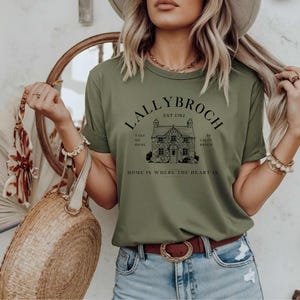 May include: A green t-shirt with a black graphic of a house and the text "Lallybroch Est 1702 Take Me Home To Lallybroch Home Is Where The Heart Is".