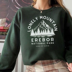 May include: A dark green sweatshirt with a white graphic design of a mountain range with trees and the text "Lonely Mountain Erebor National Park Sons of Durin".