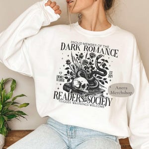 Könnte beinhalten: Weißes Sweatshirt mit schwarzem Grafikdesign. Das Design zeigt einen Schädel, eine Schlange, Rosen und den Text "Proud Member of the Dark Romance Readers Society". Der Text enthält auch "Enemies to Lovers" und "Trigger Warnings Welcome".