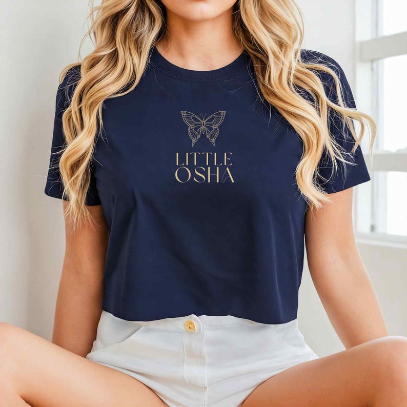 May include: A navy blue cropped t-shirt with a gold outline of a butterfly and the text "LITTLE OSHA" on the front.