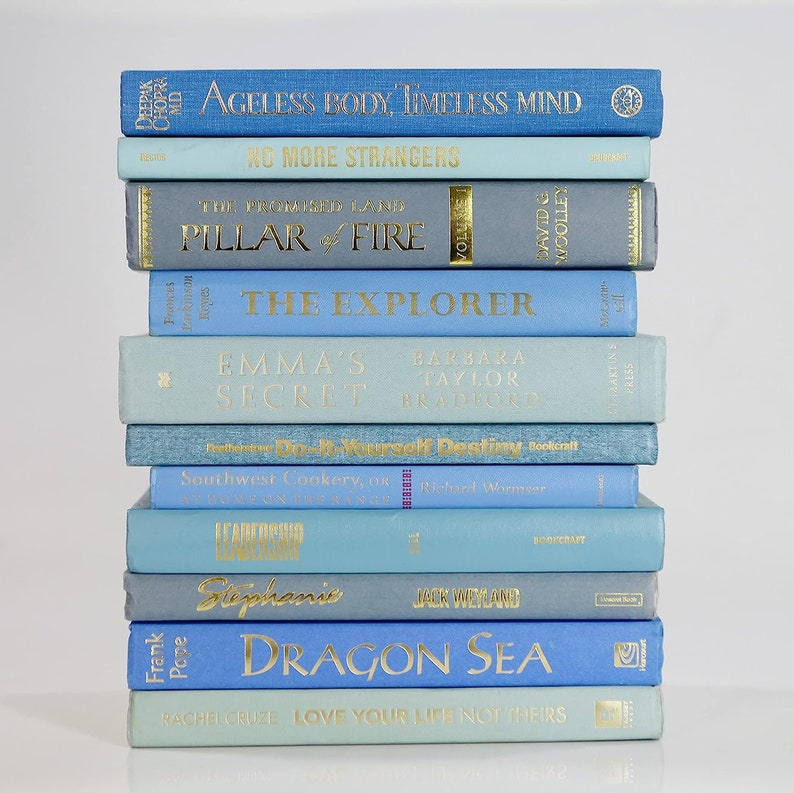 Op de afbeelding: Een stapel van 12 blauwe en lichtblauwe hardcover boeken met gouden letters op de ruggen. De titels van de boeken zijn: "Ageless Body, Timeless Mind", "No More Strangers", "The Promised Land", "Pillar of Fire", "The Explorer", "Emma's Secret", "Do-It-Yourself Destiny", "Southwest Cookery, or", "Leadership", "Stephanie", "Dragon Sea", en "Love Your Life Not Theirs".