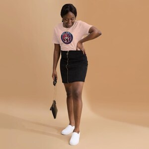 以下が含まれることがあります： 3人の女性と「Girls Trip」という文字が円形に描かれたピンクのTシャツを着た女性。黒いスカートと白いスニーカーを履いています。