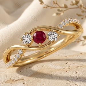 Puede incluir: Un anillo de oro con un rubí rojo central de corte redondo flanqueado por dos diamantes blancos de corte redondo. La banda tiene un diseño trenzado de estilo infinito con pequeños diamantes blancos engastados en las curvas exteriores.