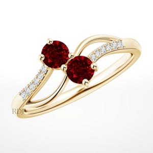 May include: A gold ring featuring two round, deep red gemstones and a series of small, clear gemstones. The ring has a flowing, elegant design, with the gemstones set in a delicate, curved band. The ring is a piece of jewelry.