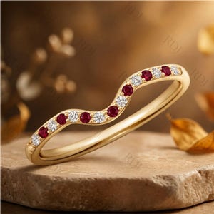 May include: A curved gold band ring featuring an alternating pattern of round-cut red rubies and clear white diamonds set along the top half of the band. The ring has a polished finish and a smooth, solid gold shank that follows a gentle wave shape.
