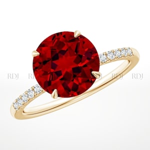 May include: A gold ring featuring a large, round, faceted red gemstone. The band is also gold and has small, clear gemstones set into it. The ring is a classic design, suitable for various occasions.