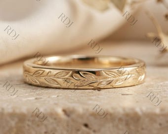May include: A gold band ring featuring a continuous engraved leaf pattern around the exterior surface. The metal has a polished finish, and the design consists of repeating vine-like motifs with small, pointed leaves etched into the gold.