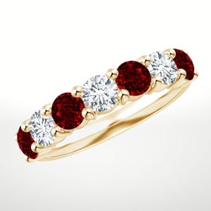May include: A gold ring with a band set with alternating red and clear gemstones. The gemstones are round-cut and set in individual prongs, creating a classic design.