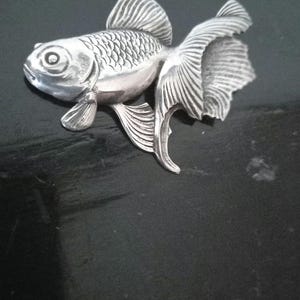 May include: A silver-colored goldfish figurine with detailed scales and fins. The figurine is a decorative piece with a realistic design.