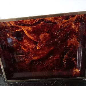 Könnte beinhalten: Ein rechteckiges Tablett mit einem goldenen Metallrahmen und einer marmorierten Oberfläche in Rot, Orange und Braun.