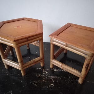Könnte beinhalten: Zwei kleine Holzstühle mit hellbrauner Oberfläche und natürlicher Maserung. Einer hat eine sechseckige, der andere eine quadratische Sitzfläche. Beide haben Beine im Bambus-Stil. Sie stehen auf dunklem Untergrund vor einer weißen Wand.