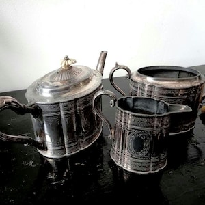 Puede incluir: Un juego de té de plata con tetera, jarra de crema y azucarero. El juego tiene un diseño ornamentado y está en buen estado.