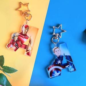 Peut inclure: Deux porte-clés avec des motifs de super-héros. L'un représente Iron Man en rouge et or, l'autre Captain America en bleu, blanc et rouge. Les deux ont la forme de la lettre "A" et sont dotés d'un fermoir en forme d'étoile.