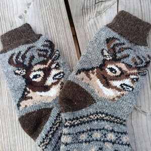 May include: A pair of gray knit socks with a deer head design on the front. The socks have brown heels, toes, and cuffs. The deer is brown and white, with a detailed antler design. The lower portion of the socks features a geometric pattern.