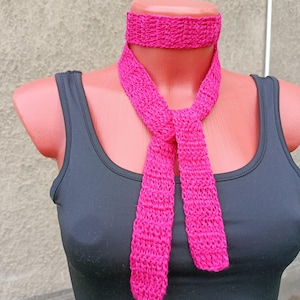Könnte beinhalten: Ein leuchtend fuchsiafarbenes Häkel-Halsband mit einem passenden langen, schmalen, schalartigen Band, das vorne herabhängt. Das Accessoire wird auf einer Schaufensterpuppe mit einem schlichten schwarzen Tanktop präsentiert und zeigt die Textur des Garns.