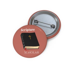 Puede incluir: Un botón redondo con fondo melocotón. Presenta la palabra "Scripture" sobre un libro negro con una cruz dorada y la palabra "SCHOLAR" debajo. El libro tiene un marcador rojo y el texto "CYCLE 2:25-26".