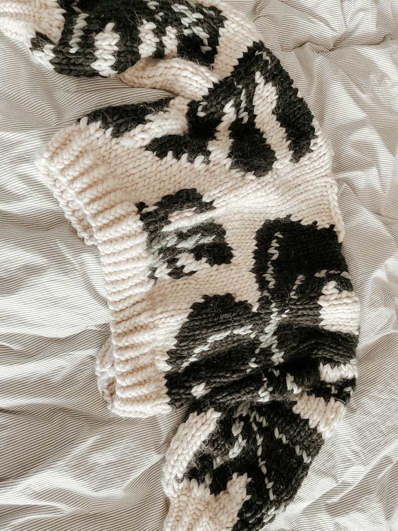 Peut inclure: Un pull en tricot cr&egrave;me avec un motif abstrait noir et blanc. Le pull est ample et a une texture tricot&eacute;e &eacute;paisse.