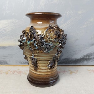 May include: A handcrafted ceramic vase with a textured, organic design. The vase features a gradient of brown and tan hues, with a dark, textured band around the middle. The top and base are a darker brown.
