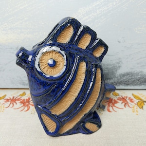 May include: A blue and brown ceramic fish figurine with a large eye and textured details.