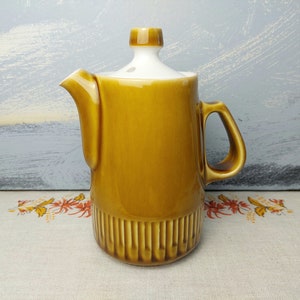May include: A brown ceramic creamer with a white lid and a ribbed design. The creamer has a handle and a spout.