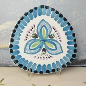 May include: A white ceramic plate with a blue and green floral design. The plate is triangular in shape and has a scalloped edge.