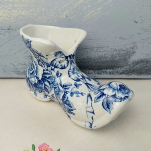 Peut inclure: Un pot de fleurs en céramique blanche en forme de botte avec un motif floral bleu. La botte est de forme sabot hollandais traditionnel.