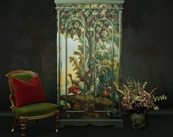 May include: A green painted wooden cabinet with two doors. The doors are decorated with a painted scene of a forest with birds and trees. The cabinet is standing on a dark floor.