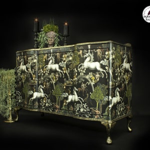 May include: A black and gold dresser with a white unicorn and floral pattern. The dresser has six drawers and sits on four legs. The dresser is decorated with a faux plant and candles.