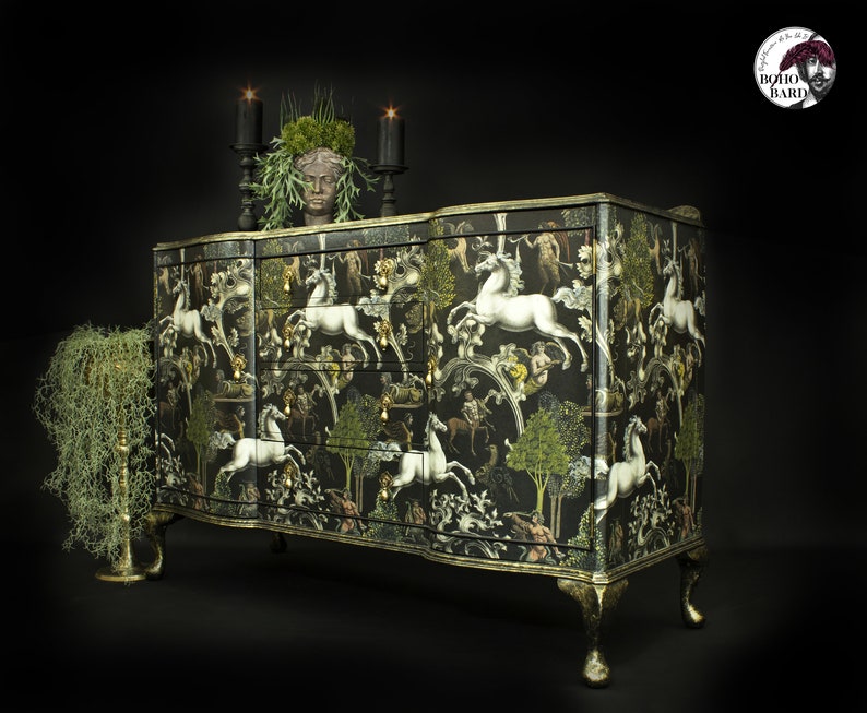 May include: A black and gold dresser with a white unicorn and floral pattern. The dresser has six drawers and sits on four legs. The dresser is decorated with a faux plant and candles.