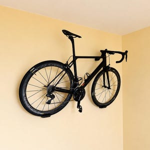 Peut inclure: Un vélo de route noir monté sur un mur. Le vélo a un design élégant et moderne avec un guidon incurvé, une selle noire et des roues noires. Le vélo est monté sur un mur jaune clair.
