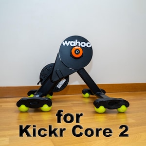 以下が含まれることがあります： フライホイールに「wahoo」の文字が入った、黒とグレーの固定自転車トレーナー。 トレーナーは黒いフレームに黄色のアクセントがあり、「for Kickr Core 2」の文字が入っています。