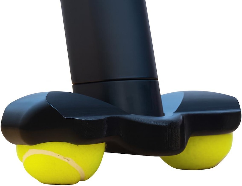 May include: A black walker glide attachment featuring two bright yellow tennis balls secured into a molded plastic base. The device is designed to fit onto the bottom of a walker leg, with the tennis balls providing a smooth surface for movement.