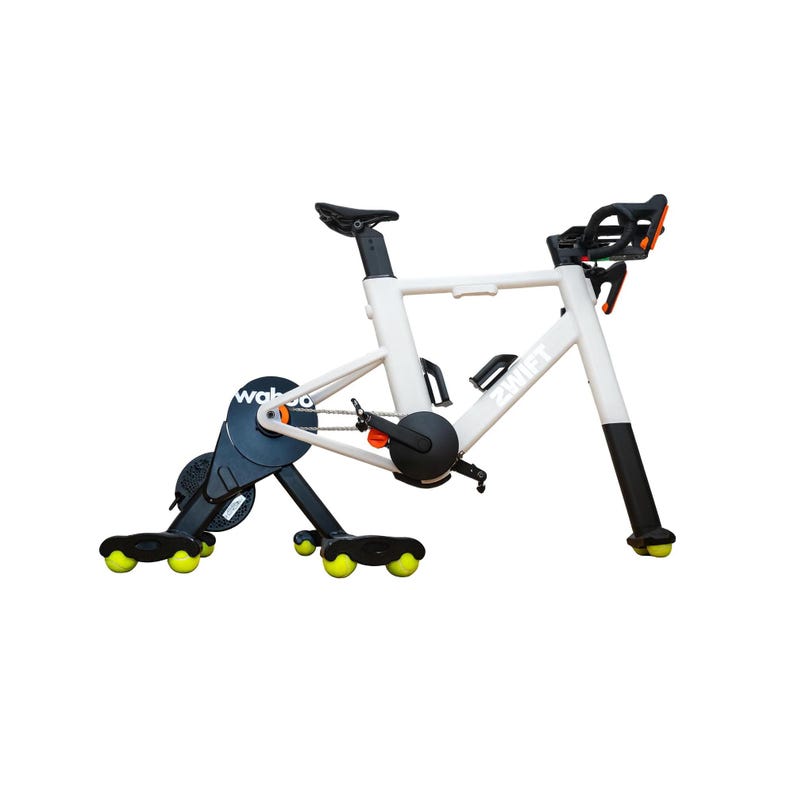 May include: A white indoor stationary bike with black accents, featuring the Wahoo logo on the rear drive unit and Zwift branding on the frame. The bike is supported by a black base with bright yellow tennis balls attached to the feet.