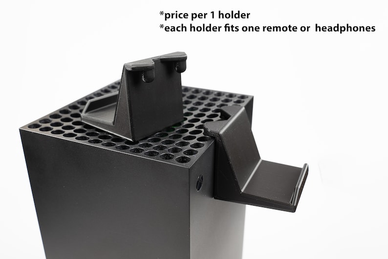 May include: Two black plastic holders for a video game console. The holders are designed to fit on the side of the console and can hold a remote or headphones. The text "*price per 1 holder *each holder fits one remote or headphones" is visible in the image.