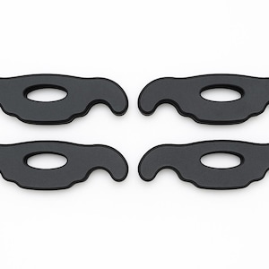 May include: A set of four identical black matte components, each featuring a symmetrical, curved silhouette with a central oval cutout and two downward-facing hook-like extensions on either side, arranged in a two-by-two grid formation.