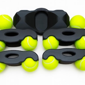 May include: A set of five black plastic furniture leg coasters, each featuring two circular cutouts designed to hold bright yellow tennis balls. The coasters are arranged in a group, with four units holding two tennis balls each and one unit empty.