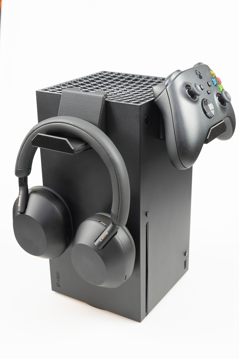 May include: A black Xbox Series X console with a black wireless controller and black over-ear headphones hanging on the side. The console has a black and white logo that says "Xbox Series X".