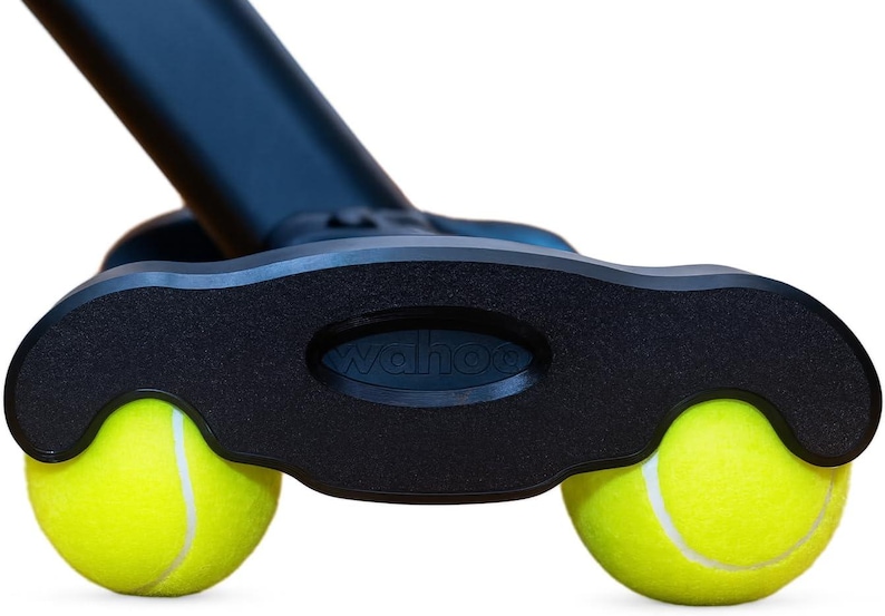 May include: A black plastic base component featuring the embossed text wahoo, designed with two circular cutouts that securely hold two bright yellow tennis balls with white seams, attached to a black angled support arm extending upwards.