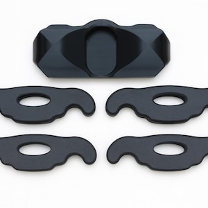 May include: A set of five black components consisting of one central rectangular piece with a smooth, contoured surface and four identical flat, wing-shaped pieces, each featuring a central oval cutout and curved, symmetrical ends.