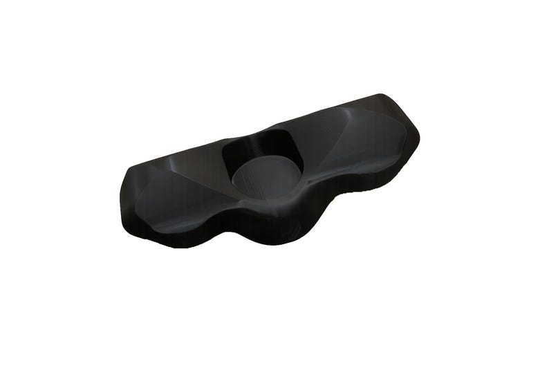 May include: A black, solid, elongated object with a smooth, contoured surface featuring a central circular indentation. The piece has an irregular, organic shape with rounded edges and a glossy finish, appearing as a singular, molded component.