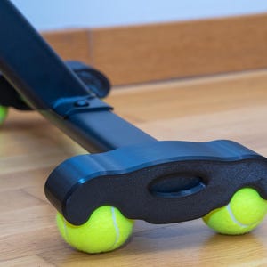 May include: A black furniture leg base featuring two bright neon yellow tennis balls fitted into the underside of the support structure to provide a protective glide for the furniture piece against the floor surface.