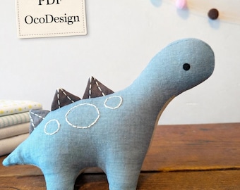 May include: A light blue stuffed dinosaur toy with brown accents and white stitching. The dinosaur has a long neck, a small black eye, and three brown triangular spikes on its back. The text "PDF OcoDesign" is on a tag.