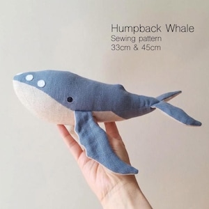 Może przedstawiać: Wykrój do szycia humbaka z niebieskiej i beżowej tkaniny z białymi okrągłymi akcentami na głowie i ciemnym okiem. Tekst brzmi Humpback Whale Sewing pattern 33cm & 45cm. Ta miękka rzeźba charakteryzuje się dwukolorowym wzorem z niebieską górą.